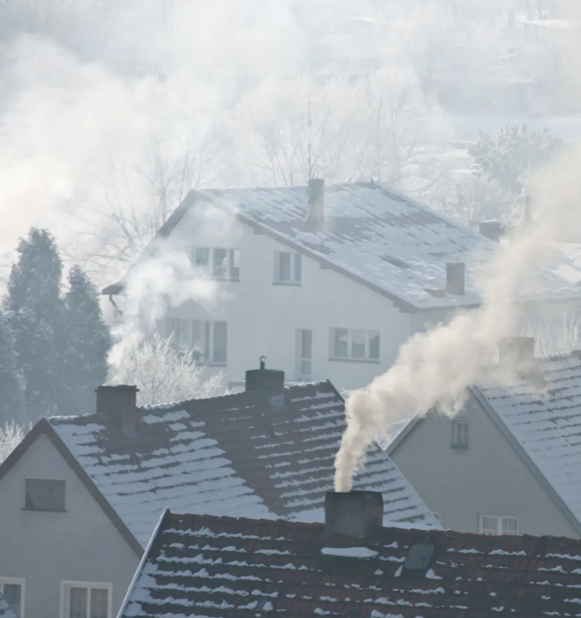 Zdjęcie przedstawia kominy domów z dymem