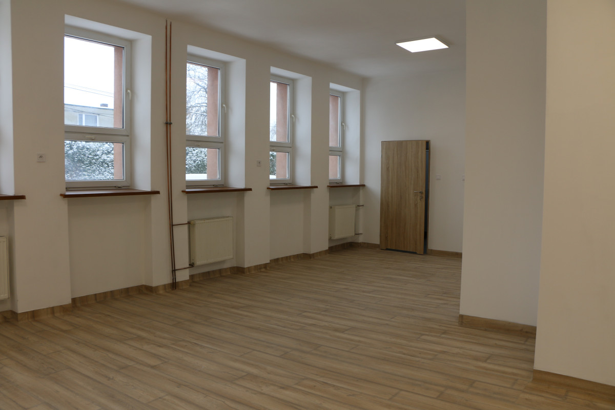 Fotografia przedstawia puste pomieszczenie, białe ściany, podłoga panele drewniane, okna