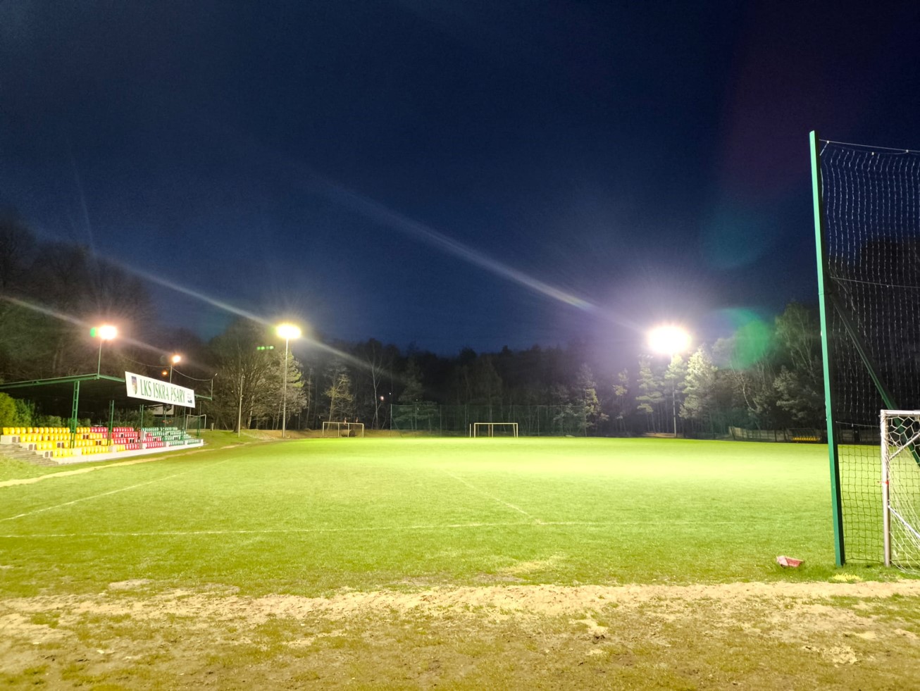 Zdjęcie przedstawia stadion LSK Iskry Psary po zmroku, oświetlony